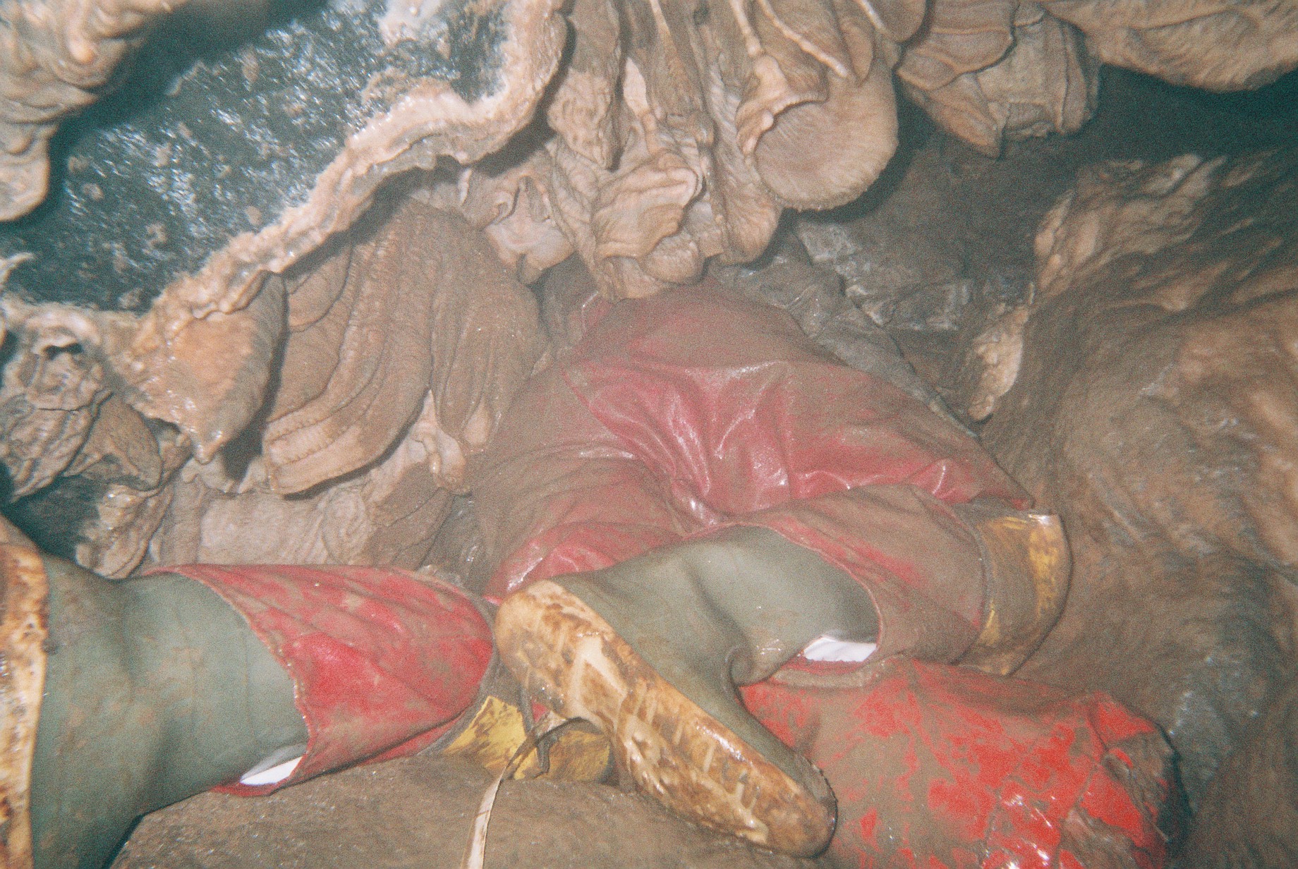 A well-decorated cave passage with a caver squeezing through flowstone